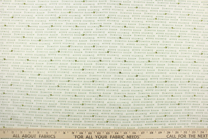 This quilting fabric feature  a Downtown Abbey print with a bit of holly in green against a white background .