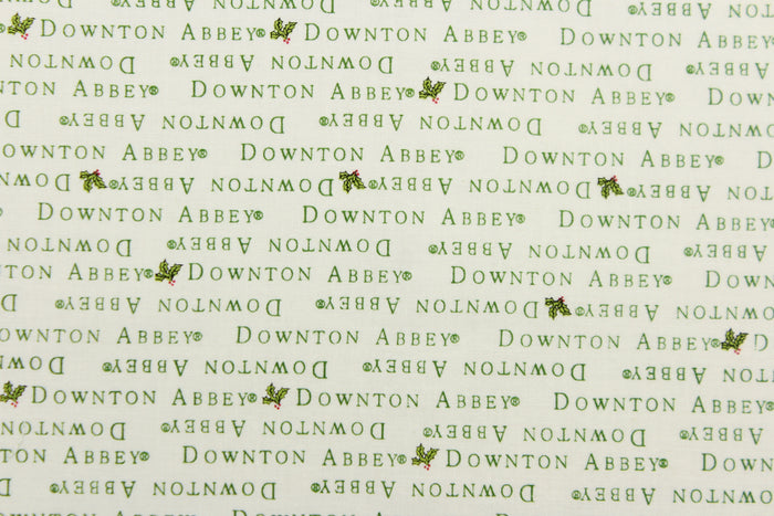 This quilting fabric feature  a Downtown Abbey print with a bit of holly in green against a white background .