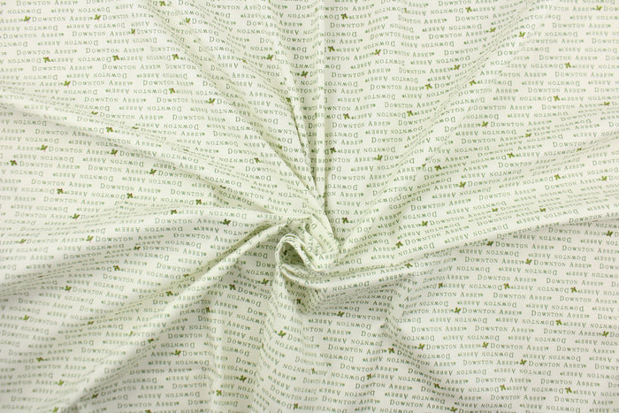 This quilting fabric feature  a Downtown Abbey print with a bit of holly in green against a white background .