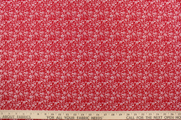 This fabric features a whimsical vine and floral design in white set against a red background.