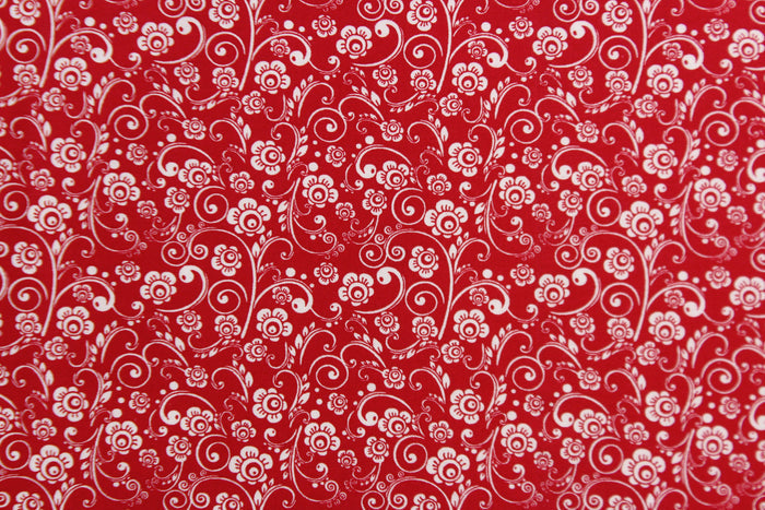 This fabric features a whimsical vine and floral design in white set against a red background.