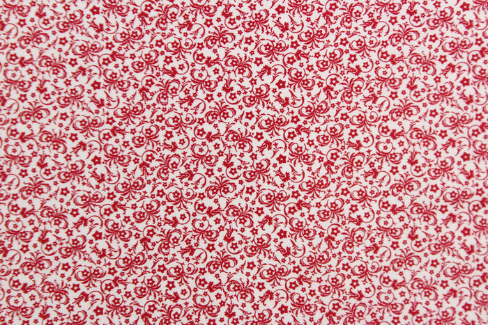 This fabric features a tiny floral design in red set against a white background.