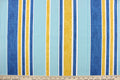 This outdoor fabric features a stripe design in blue, white, golden tan, and aqua.