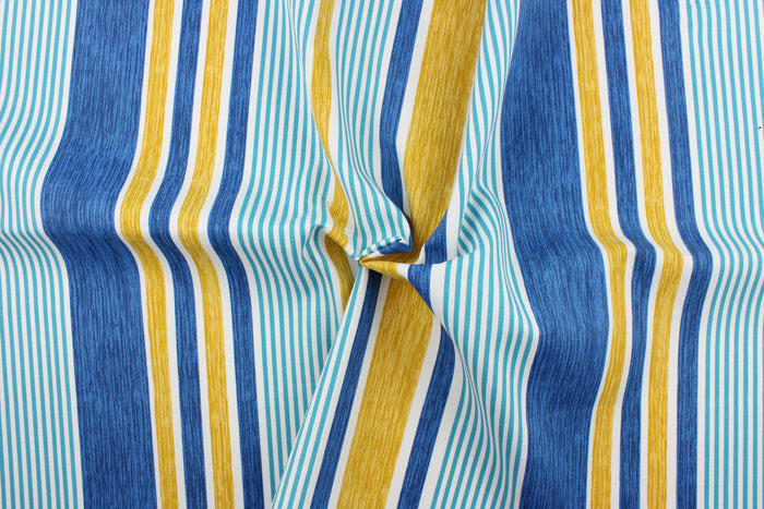 This outdoor fabric features a stripe design in blue, white, golden tan, and aqua.