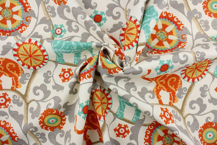 Menagerie is an outdoor fabric featuring suzani medallions and elephants in aqua, gold, gray, orange, red and tan against a cream background.