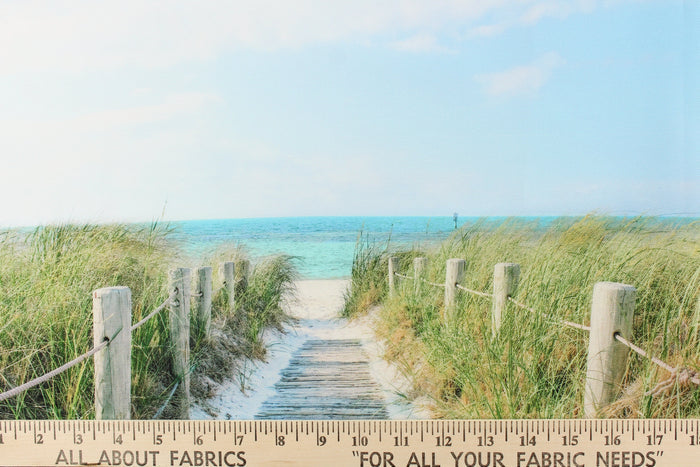 This fabric features a beautiful realistic view of a boardwalk out through the sand dunes to the ocean in beige, blue, green and gray.