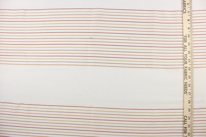 This sheer fabric features a stripe design in orange, brown, red, and golden yellow  against white.