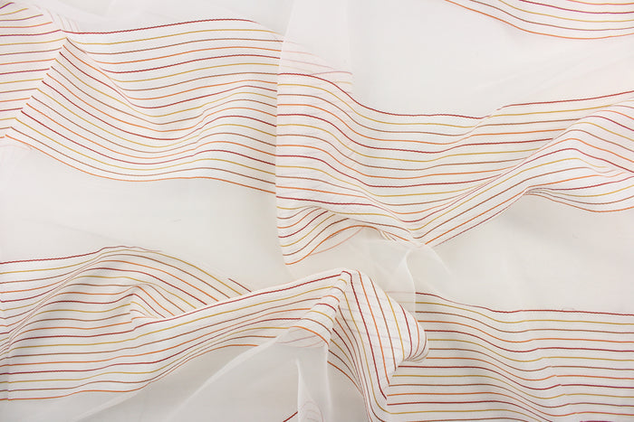 This sheer fabric features a stripe design in orange, brown, red, and golden yellow  against white.