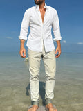 Man standing on a beach wearing a white shirt and light-colored pants.