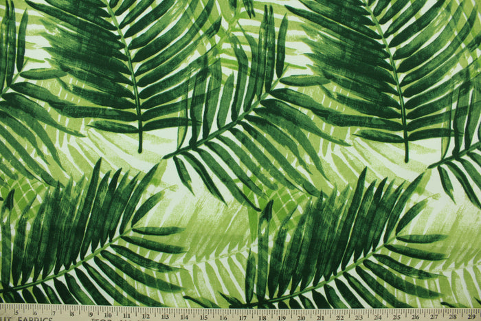 This outdoor fabric features a tropical leaf design in shades of green set against a white background.