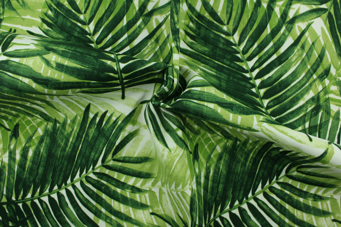 This outdoor fabric features a tropical leaf design in shades of green set against a white background.